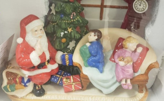 Figurines of Santa Clause handing gifts to a boy and girl in pajamas on a sofa