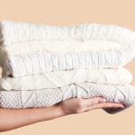 Person holding out a stacked pile of fall / winter sweaters in neutral colours to as a donation of gently used clothing goods