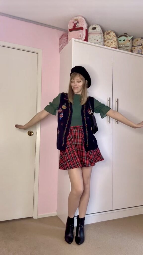 Jade wearing a thrifted green blouse with plaid skirt, black beret, boots, and vest