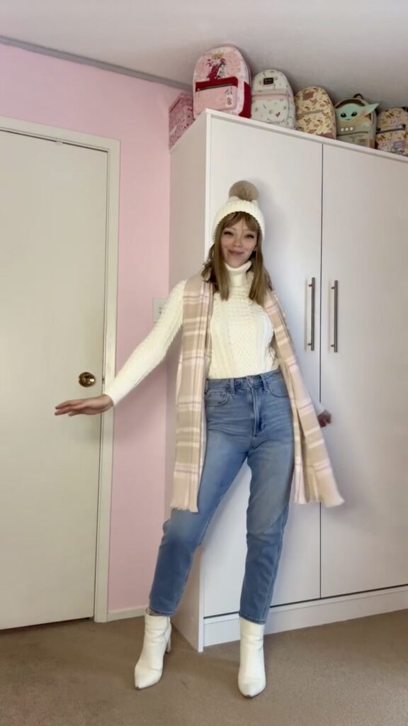 Jade wearing a thrifted white knit sweater with winter hat and boots, denim, and neutral vest