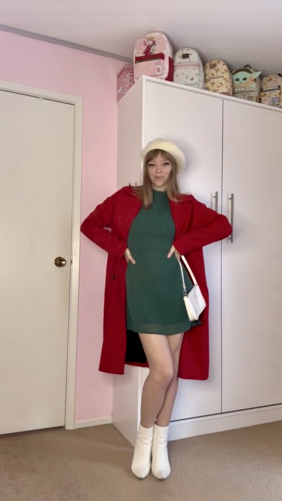 Jade wearing a thrifted red trench coat with green dress, white boots, beret and purse
