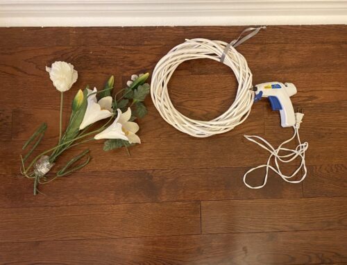 Artificial lilies, white wreath, and hot glue gun laying on table for spring DIY project