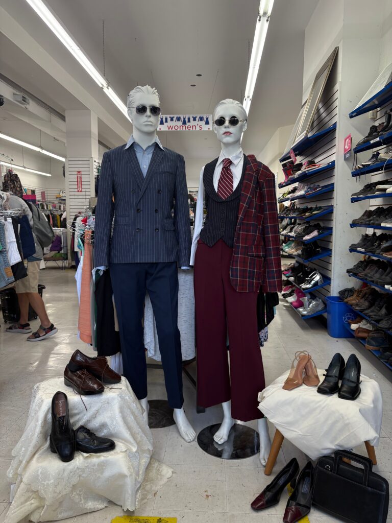 workwear outfits including blazer, dress shirt, and sunglasses on a male mannequin and a vest, tie, collar top, and sunglasses on a female mannequin featured inside Thrift Store