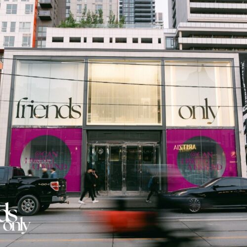 Zara storefront with window panels saying friends only. Cars passing by and people walking in front of the store square crop